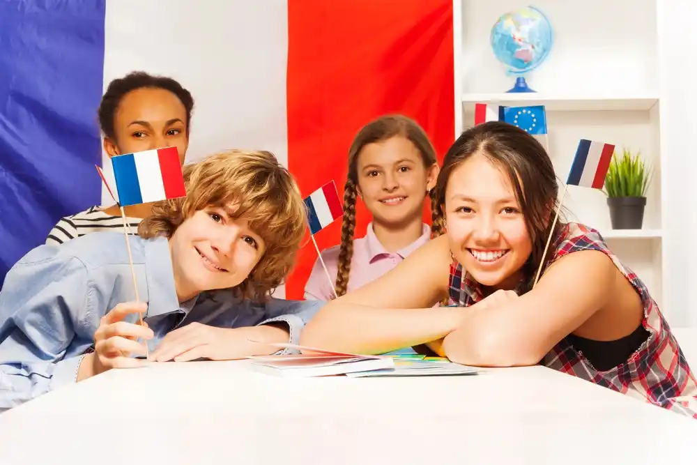 Four diverse students smile, holding small french flags; learning french.