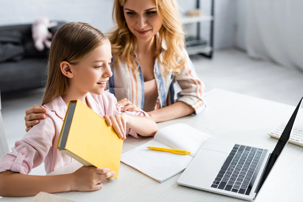 Mother and daughter studying together at home, using laptop and books.