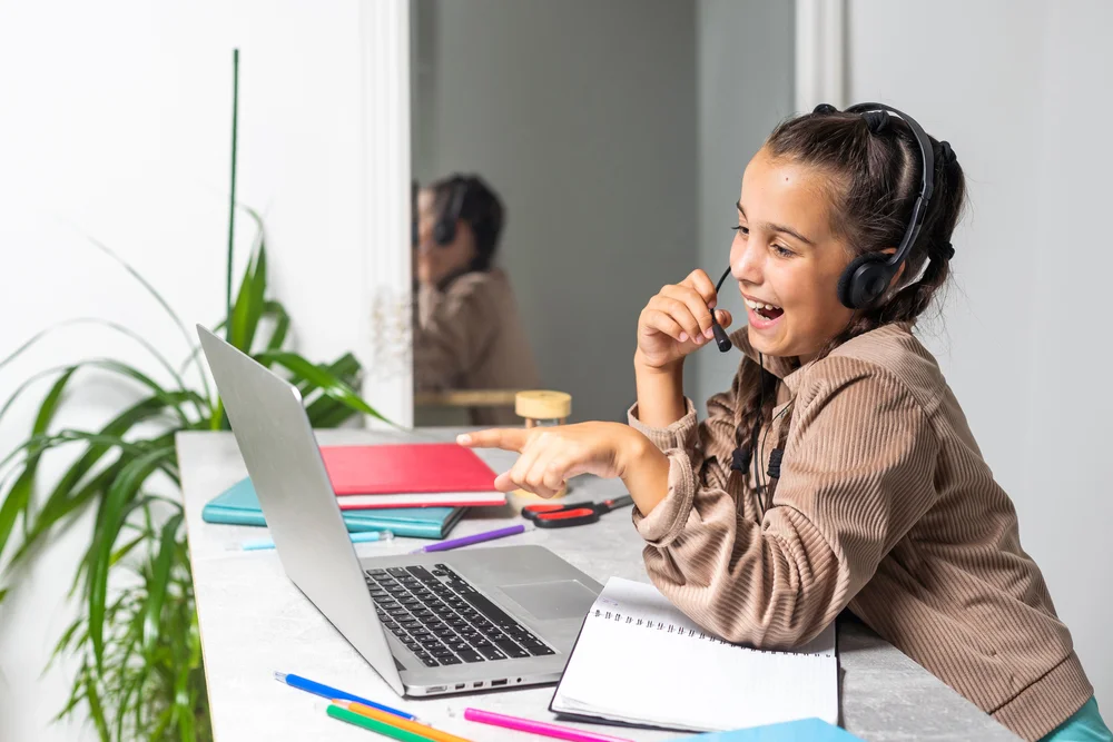 Happy girl wearing headset, using laptop for online learning.